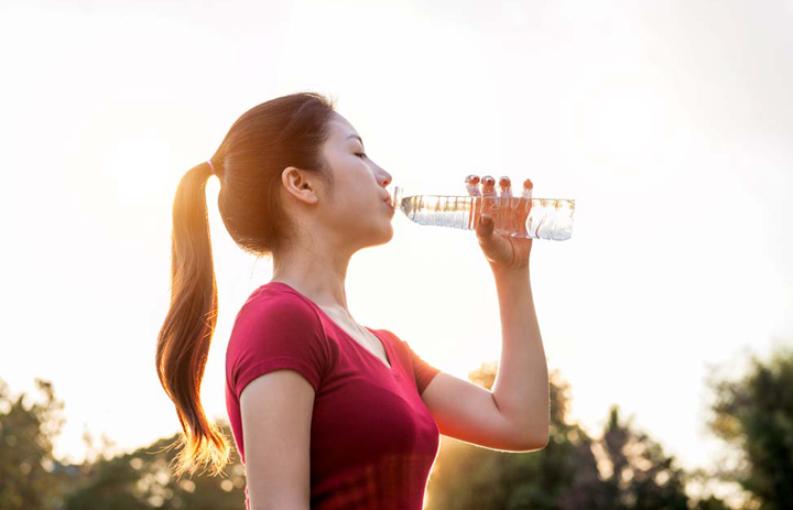 Sporty woman drinking water on sunlight.